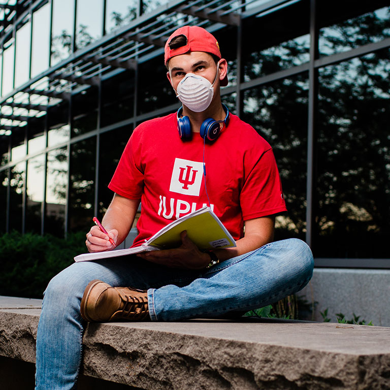 A student with his mask writing in his notebook.